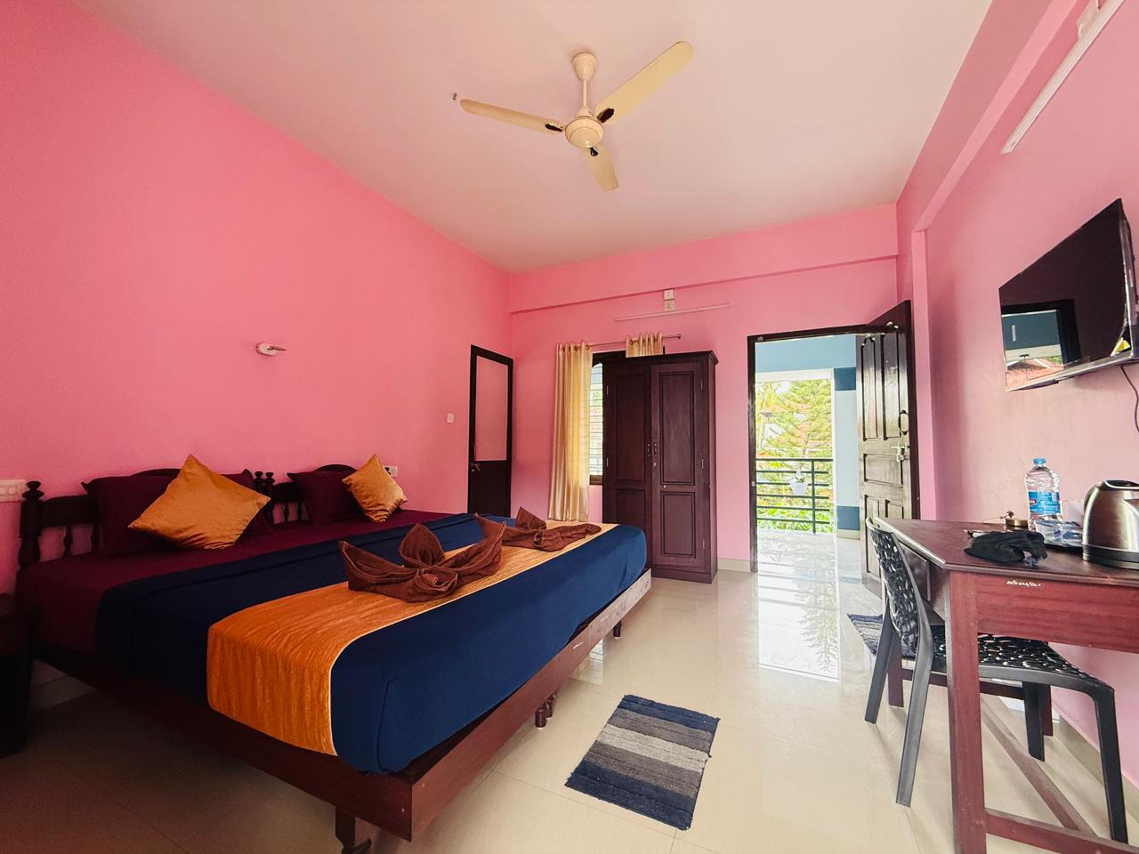 Guest room with blue and orange bedding, desk, and balcony door